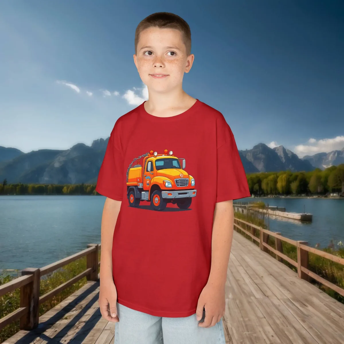 Boy in dark red t-shirt with cartoon orange tow truck graphic, standing near lake