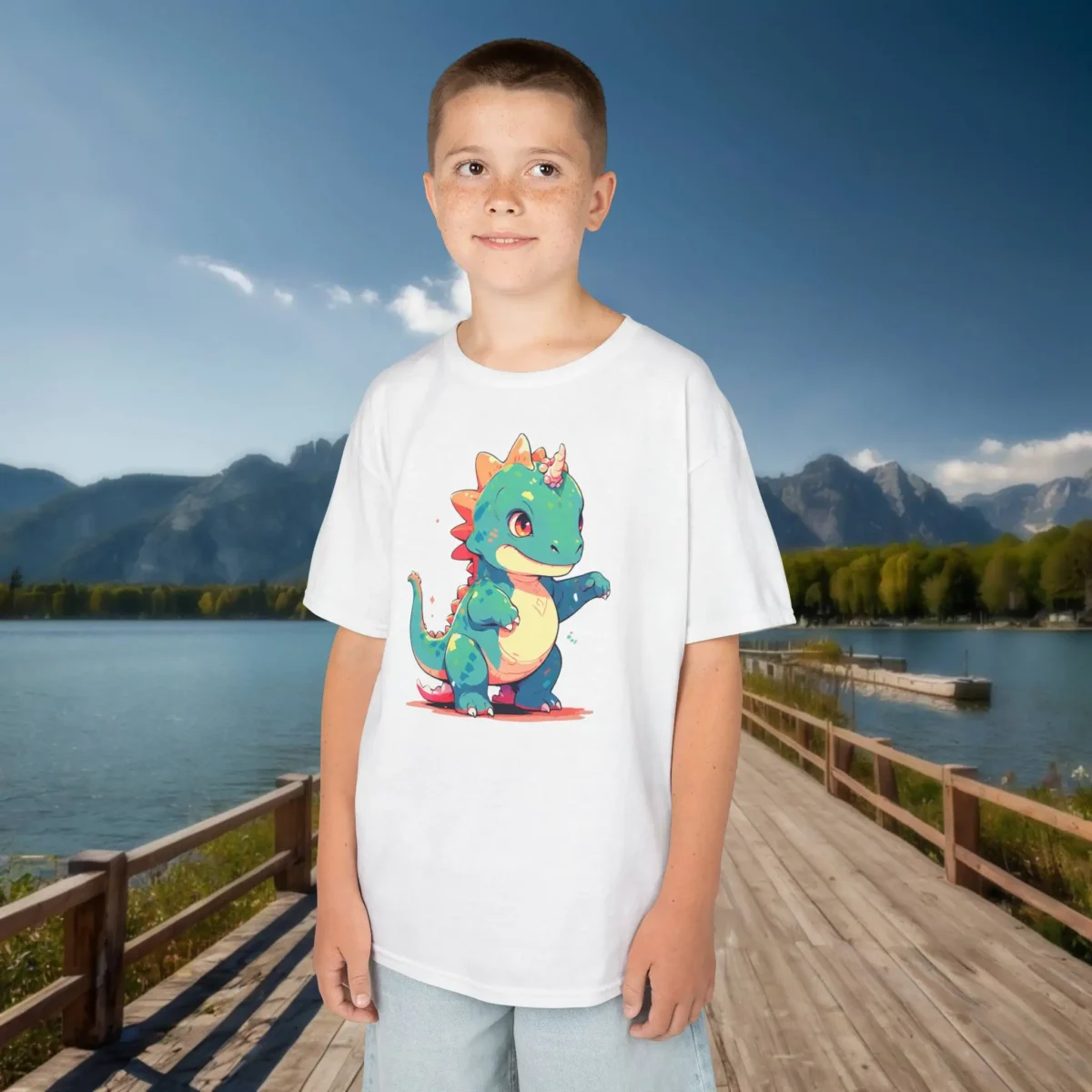 Smiling boy wearing a white t-shirt with a playful cartoon baby Iguanodon featuring colorful details and a unicorn horn.