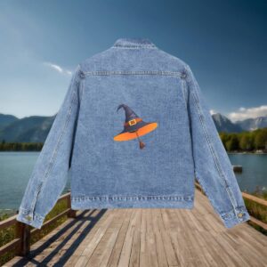 Flat-lay of a denim jacket featuring a witch's hat graphic on the back, placed on a dock with lake and mountains in the background.