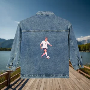 Flat view of a denim jacket with an illustration of a female soccer player kicking a ball.