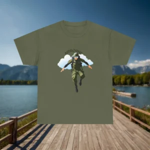 Flat lay of an army green Airborne graphic t-shirt with a paratrooper design, displayed on a wooden dock with a lake and mountains in the background.