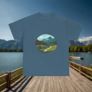 Blue t-shirt with a circular mountain and forest landscape design displayed on a wooden dock by a lake