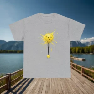 Grey t-shirt with a yellow pickleball and paddle graphic design displayed on a wooden dock with mountain scenery