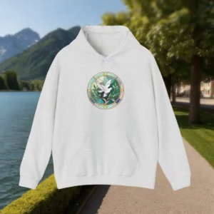 Light grey hoodie with a Christian stained glass dove design, displayed outdoors by a mountain lake.