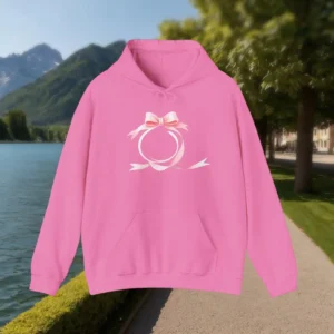 Pink hoodie with a ribbon bow design displayed outdoors near a lake and trees.