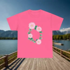 Pink t-shirt with a circular arrangement of white and pink daisies displayed on a wooden dock with lake and mountain backdrop